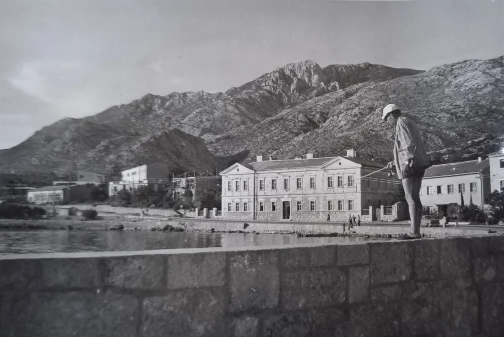 Pogled na školu u Karlobagu dok netko lovi ribe na obali