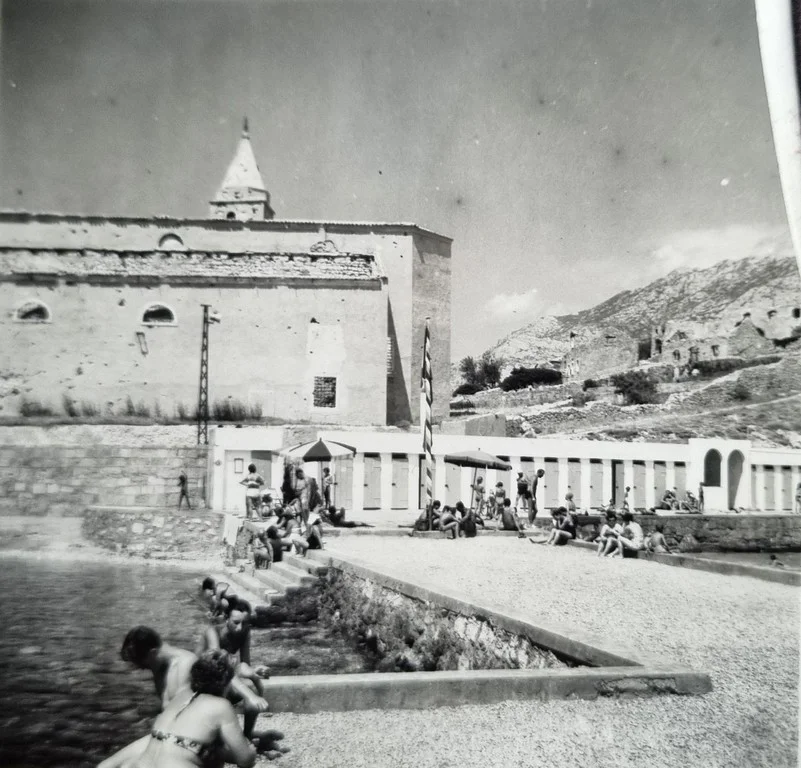 Kupači na gradskoj plaži ispred razrušene crkve u poslijeratnom Karlobagu